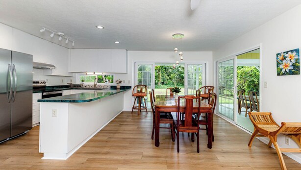 Cocina moderna con una isla grande, mesa de comedor de madera y sillas, conectada a un amplio espacio comedor con ventanas grandes.