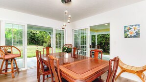 Un comedor con mesa y sillas de madera, puertas de cristal grandes que dan a un jardín, y una lámpara en el techo.