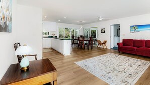 Una cocina moderna con armarios blancos, un comedor con sillas de madera, un sofá rojo y una alfombra floral grande.