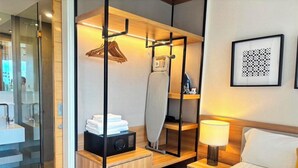 Een hotelkamer met een bed, nachtkastje, lamp en een spiegel met kledingroede.