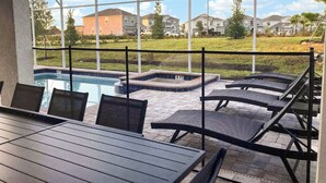 Un espacio al aire libre techado con piscina, sillas de descanso y una mesa.