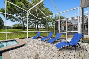 A covered outdoor area with lounge chairs, a hot tub, and a glass-enclosed building. - Game Room + Theater + Pool + Hot Tub | 15-Min Disney | Luxury 8BR Disney Villa (Davenport)