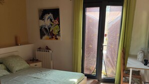 A bedroom with a bed, a nightstand, a painting, a window with curtains, and a view outside.