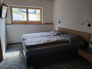 Un dormitorio con cama, ventana y lámpara fijada a la pared.
