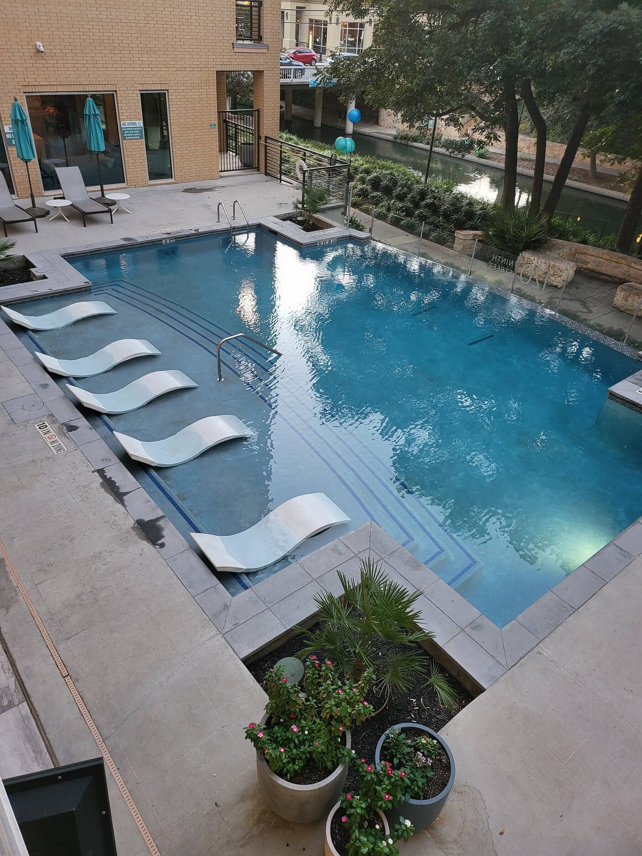A rectangular swimming pool with lounge chairs and potted plants.