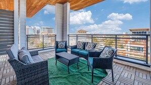A covered outdoor seating area with wicker furniture, a green rug, and a view of the cityscape. - Riverwalk Penthouse Skyline Views  RSV Parking Pet Friendly Free parking (San Antonio)