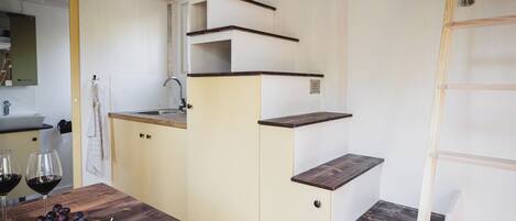 A compact kitchen with a sink, countertop, and wooden shelves.