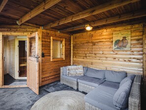 A log cabin interior with a sofa, a door leading to a bathroom, and a wall-mounted light fixture. - Vacation cottage in nature - tiny - peaceful - woods - outdoor sauna (Putten)