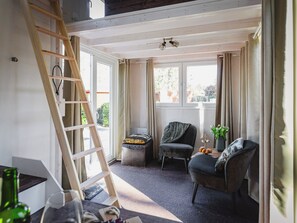 A room with a wooden ladder, two chairs, a small table with a plant, and a window with curtains. - Vacation cottage in nature - tiny - peaceful - woods - outdoor sauna (Putten)