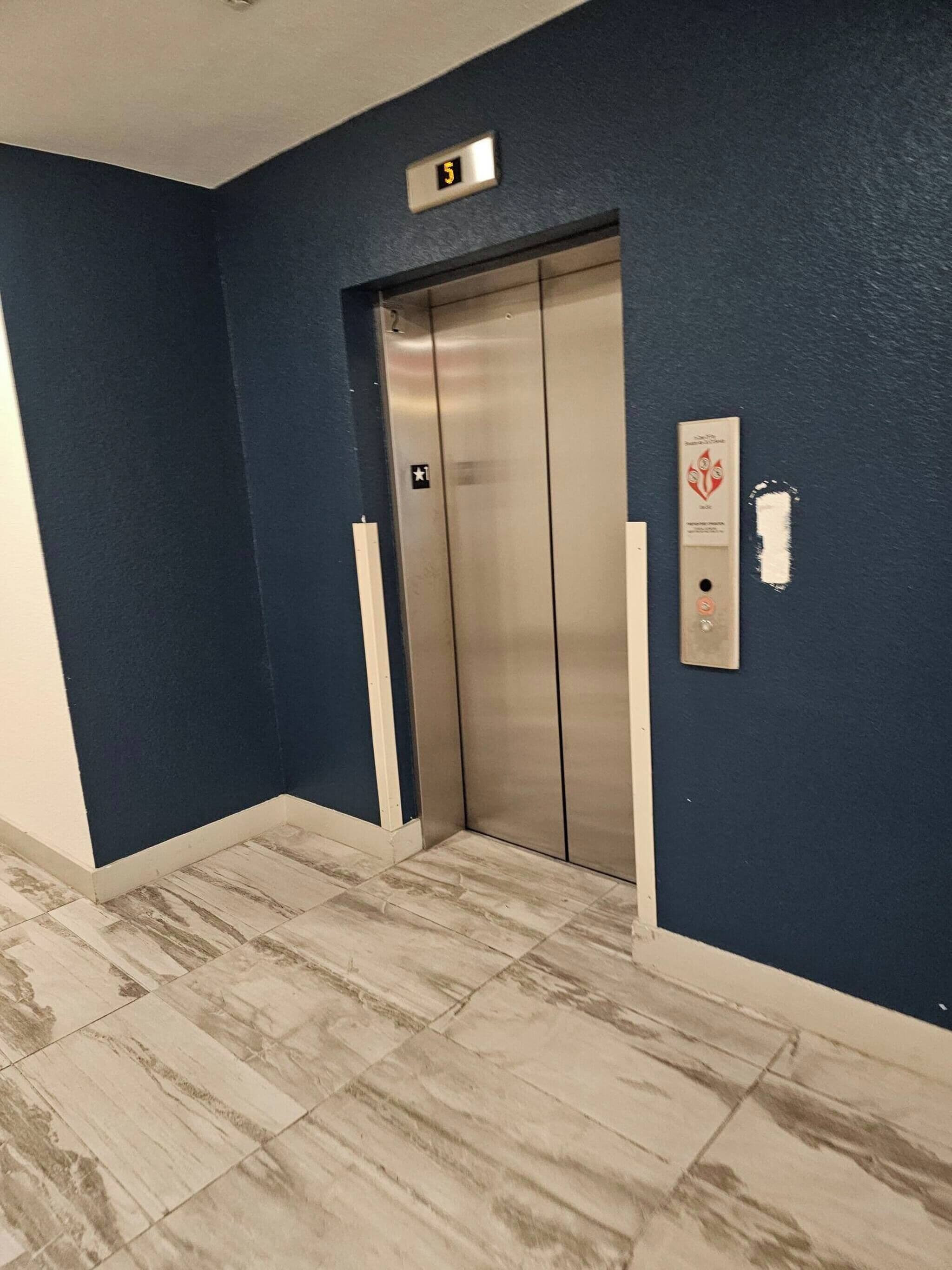 A hallway with a blue wall, an elevator, and a fire alarm panel.