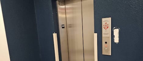 A hallway with a blue wall, an elevator, and a fire alarm panel.