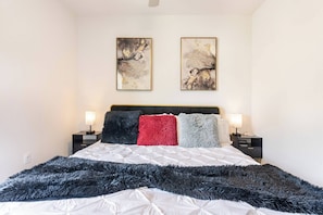 Quarto com uma cama, duas mesas de cabeceira, uma cabeceira preta e duas pinturas abstratas na parede.