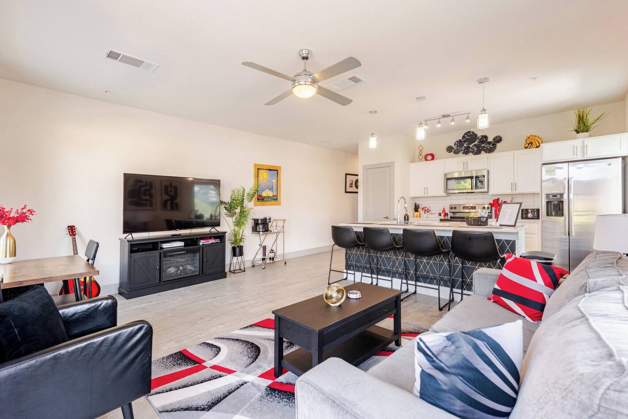 A modern living room with a sofa, coffee table, and TV. There is a kitchen area with a microwave, refrigerator, and dining space.