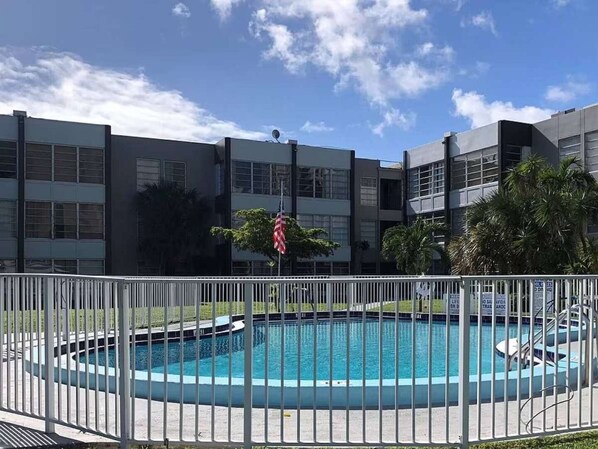 A swimming pool surrounded by a white fence, with a building in the background. - ✨Deluxe Designer Two Bedroom Apartment at Fort Lauderdale (Fort Lauderdale)