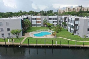 A residential building with a swimming pool surrounded by a fence, a grassy area, and a body of water in the foreground. - ✨Deluxe Designer Two Bedroom Apartment at Fort Lauderdale (Fort Lauderdale)