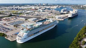 Ett stort kryssningsfartyg lade till vid en hamn, med en stadsbild som bakgrund.