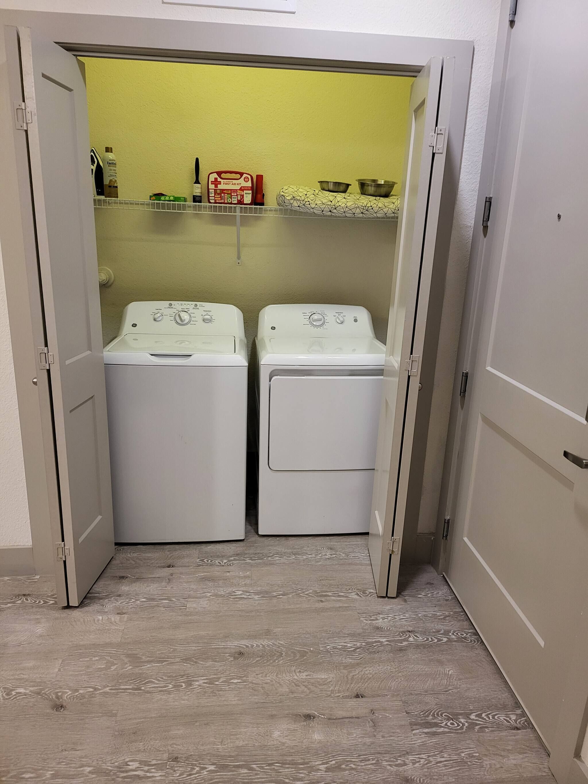 A laundry room with two white washing machines and a shelf with various items.
