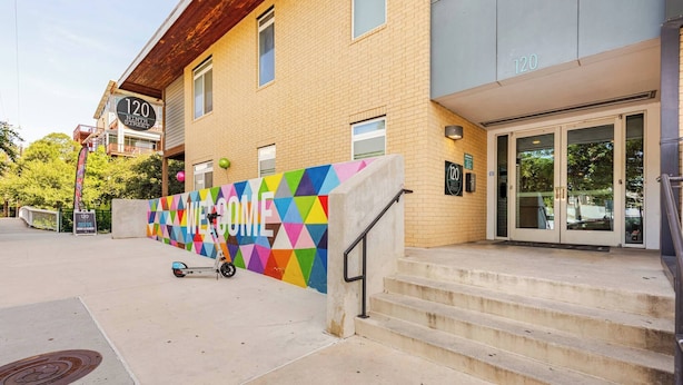 A building with a colorful geometric wall, a scooter parked in front, and a staircase leading to the entrance. - Chic Riverwalk Facing Condo Pool View  Free Parking Pets Welcome (San Antonio)