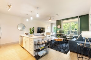 Una sala moderna con sofá, mesa de centro y televisor. Hay una cocina con pileta y alacenas.