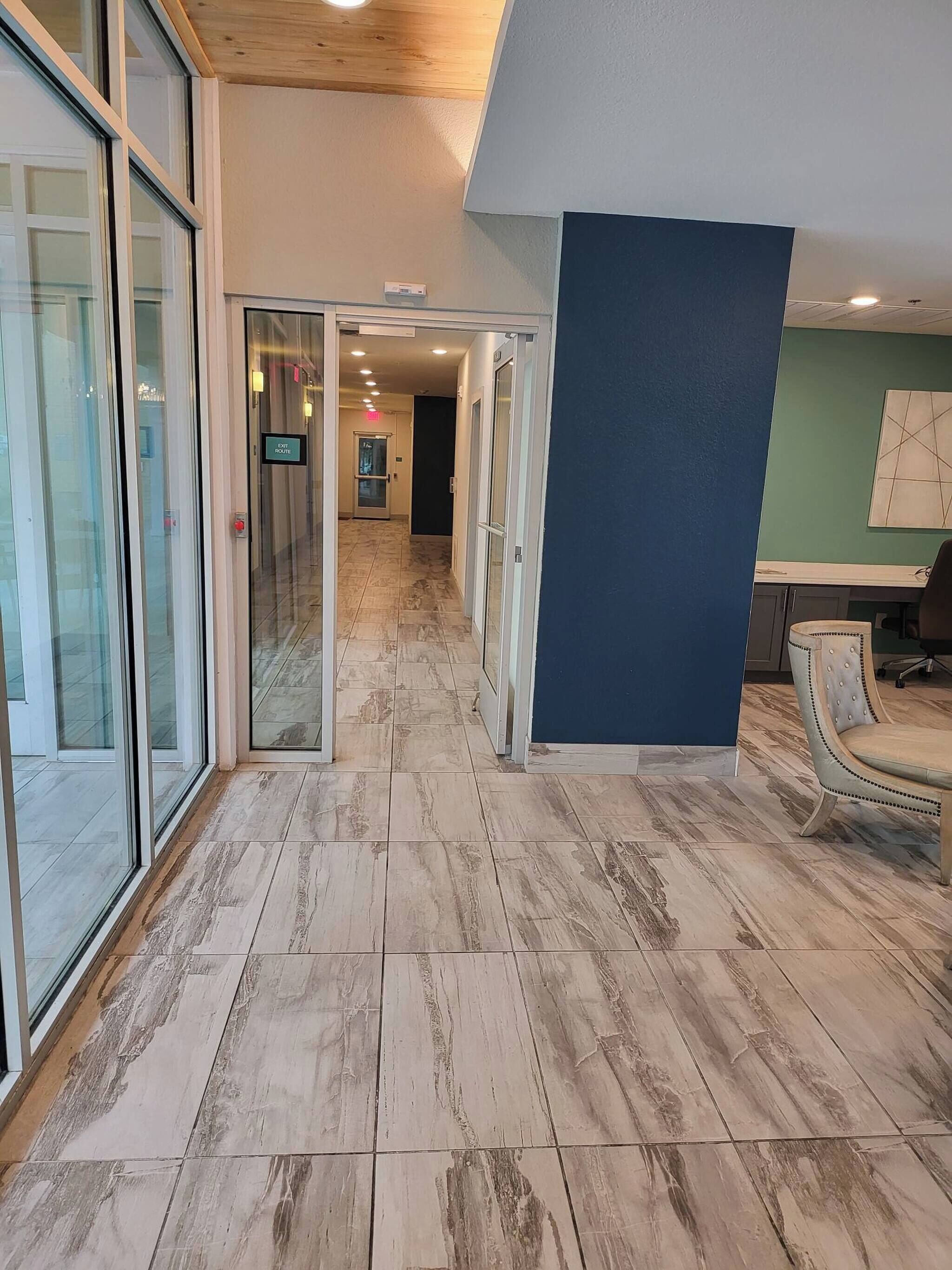 A hallway with glass doors, a blue accent wall, and a chair.