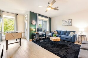 A modern living room with a foosball table, a blue sofa, a round coffee table, and a ceiling fan.