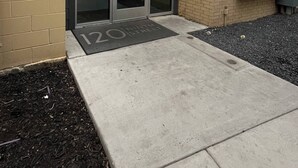 A building entrance with a glass door, a green sign above the door, and a doormat with '120 Ninth Street' on it. - Chic Riverwalk Facing Condo Pool View  Free Parking Pets Welcome (San Antonio)