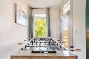 A foosball table in a room with a window, a painting on the wall, and a door.