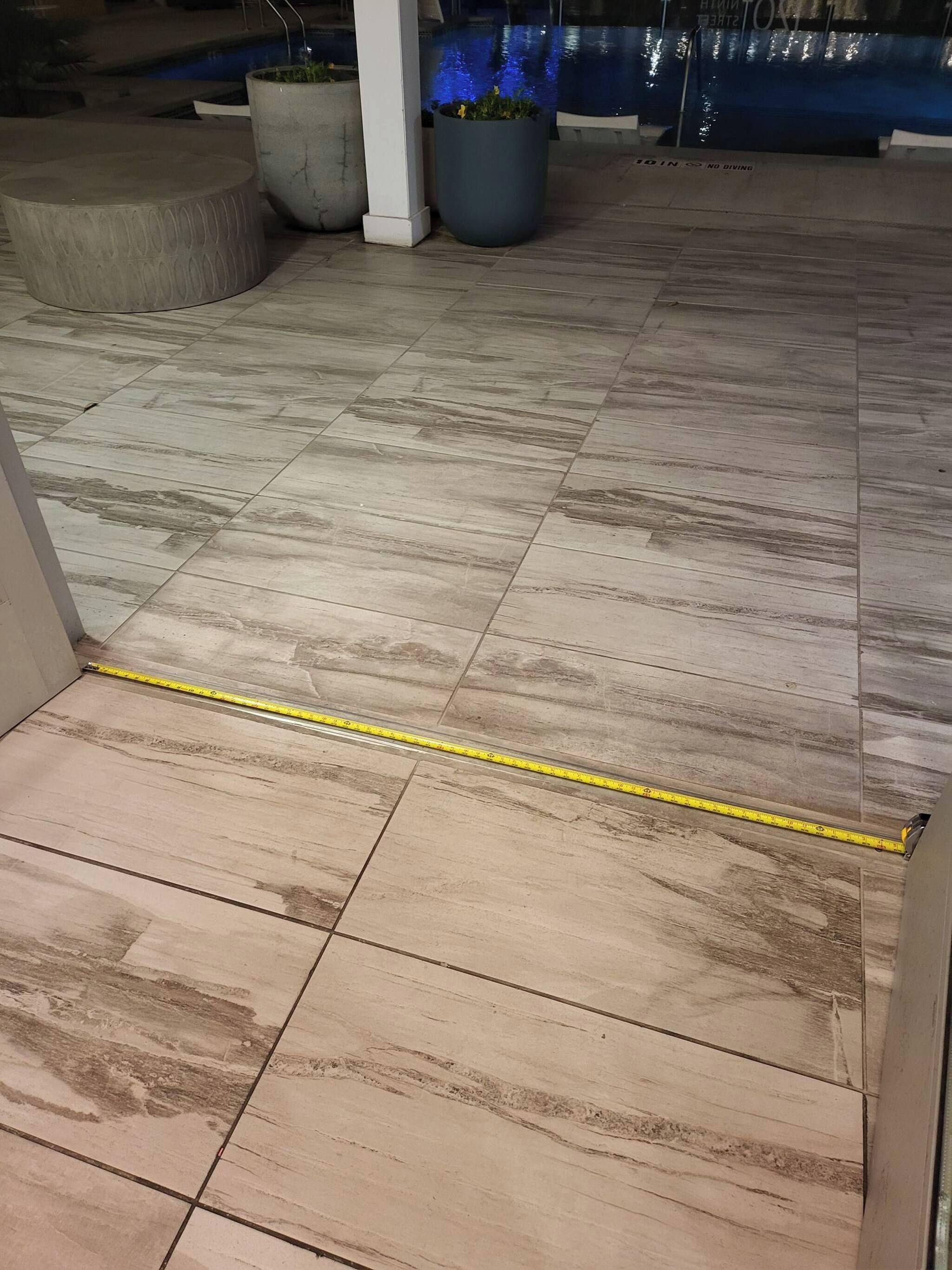 A tiled floor with a measuring tape, potted plants, and a pool in the background.