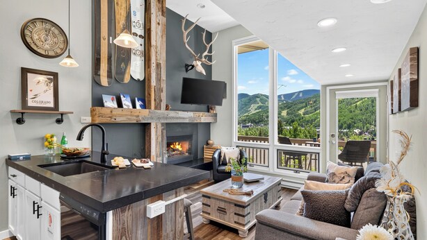 A modern kitchen with a large island, a fireplace, and a view of the mountains. - Steps to Trails + Free Bus to Slopes | Balcony + Views | Serenity by the Slopes (Vail)