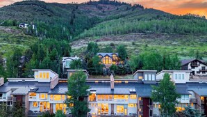A residential area with modern houses, a prominent house with large windows, and a forested hill in the background. - Steps to Trails + Free Bus to Slopes | Balcony + Views | Serenity by the Slopes (Vail)