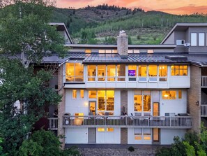 A multi-story building with large windows, balconies, and a view of a hilly landscape. - Steps to Trails + Free Bus to Slopes | Balcony + Views | Serenity by the Slopes (Vail)