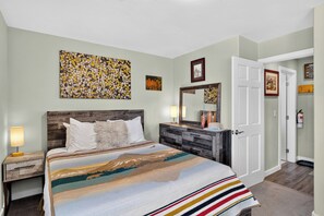 A bedroom with a bed, nightstand, dresser, and a door leading to another room. - Steps to Trails + Free Bus to Slopes | Balcony + Views | Serenity by the Slopes (Vail)