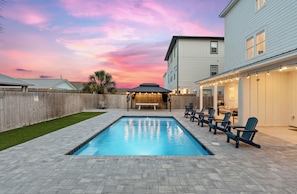 A backyard with a swimming pool, outdoor seating, and a wooden fence. - Walk to Beach • Shared Pool + Hot Tub • Near St. Andrews | Low Tide (Panama City Beach)