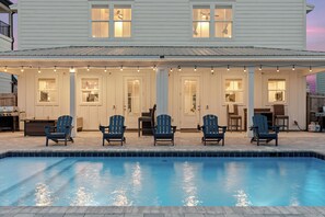 A poolside area with chairs and a pool, a covered patio with string lights, and a white building with windows. - Walk to Beach • Shared Pool + Hot Tub • Near St. Andrews | Low Tide (Panama City Beach)