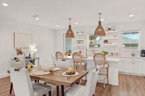 A modern kitchen with white cabinetry, a wooden dining table, and pendant lighting. - Walk to Beach • Shared Pool + Hot Tub • Near St. Andrews | Low Tide (Panama City Beach)