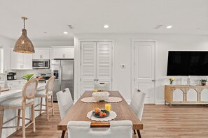 Una cocina moderna con armarios blancos, una mesa de comedor con sillas, un televisor y piso de madera.