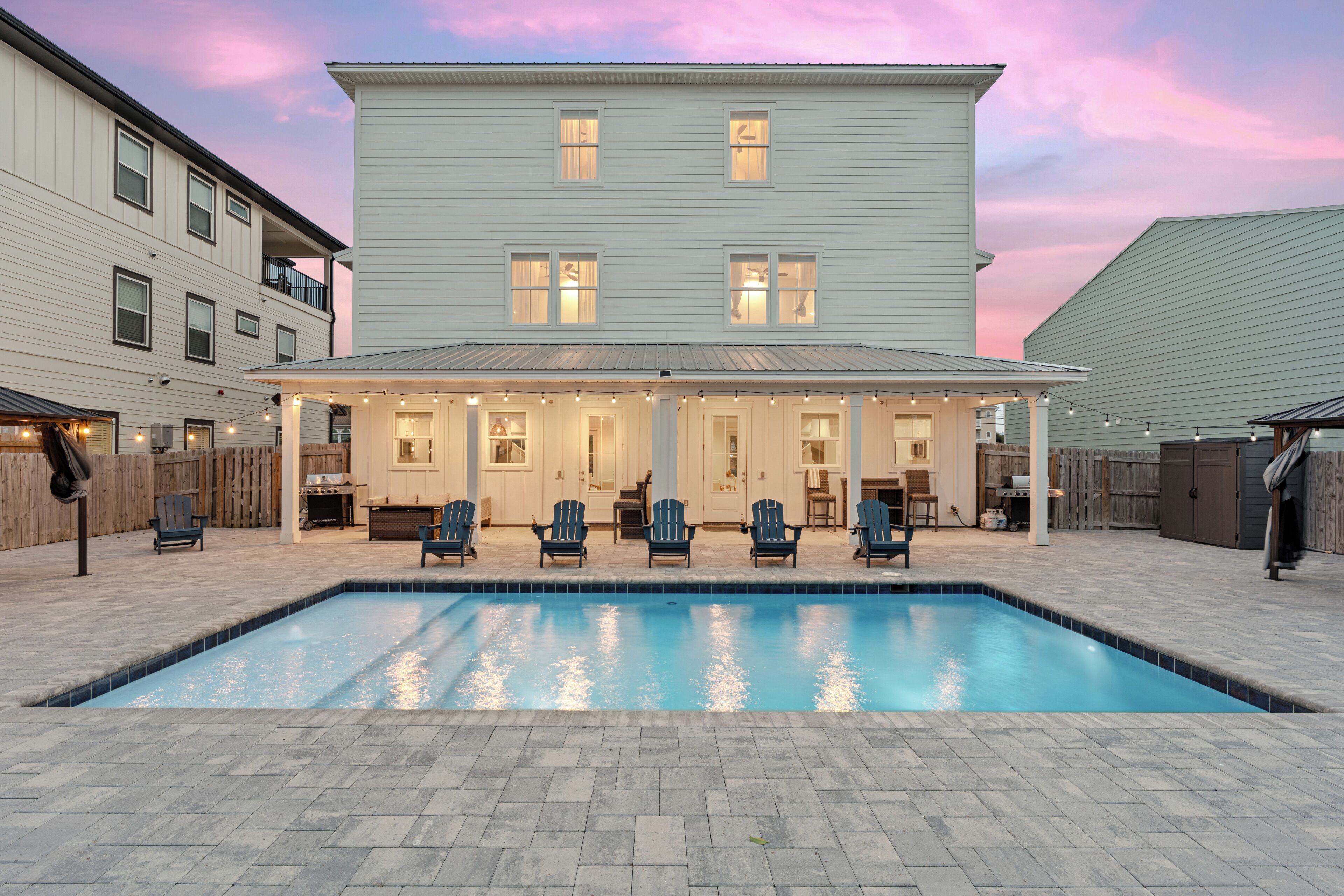 A pool with lounge chairs, a covered patio, and a two-story building with windows.