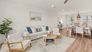 Ein modernes Wohnzimmer mit einer Couch, Sesseln, einem Couchtisch und einem Essbereich mit Tisch und Stühlen.