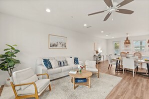 A modern living room with a sofa, chairs, a coffee table, and a dining area with a table and chairs. - Walk to Beach • Shared Pool + Hot Tub • Near St. Andrews | Low Tide (Panama City Beach)