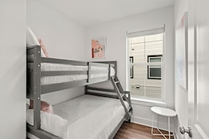 A bunk bed room with a window, a small table, and a door. - Walk to Beach • Shared Pool + Hot Tub • Near St. Andrews | Low Tide (Panama City Beach)