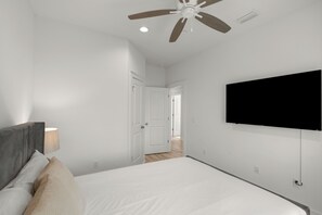 Ein Schlafzimmer mit einem Bett, einem Deckenventilator, einem an der Wand montierten Fernseher und einer Tür zu einem weiteren Raum.