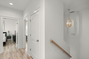 Ein Flur mit weißen Türen, einer Holztreppe und einer Hängelampe.