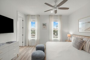 Ein Schlafzimmer mit Bett, Deckenventilator, Fernseher, Nachttisch und einem Fenster mit Vorhängen.