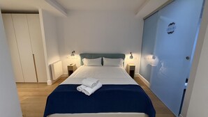 A neatly made bed with a blue blanket and white pillows, a bedside table with a lamp, and a door with a sign. - Oasis Urban Malaga in M Laga (Málaga)