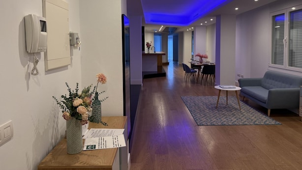 A modern hotel room with a wooden floor, a sofa, a small table with a vase of flowers, and a telephone on the wall. - Oasis Urban Malaga in M Laga (Málaga)