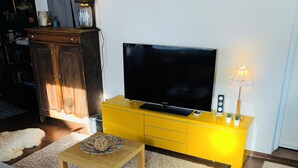 Un salon avec un canapé, une table basse, un téléviseur posé sur un meuble jaune et une lampe.