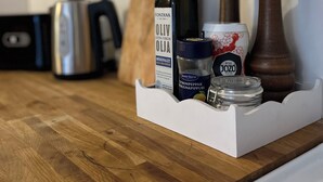 Un plan de travail de cuisine avec une bouteille d’huile d’olive extra vierge, un pot de poivre au citron de la marque Santa Mariet et un récipient de poivre de la marque Jozo.