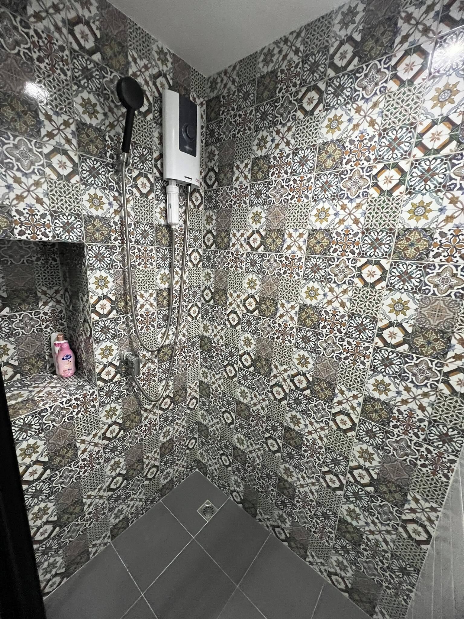 Un baño con azulejos estampados, ducha y dispensador de jabón.