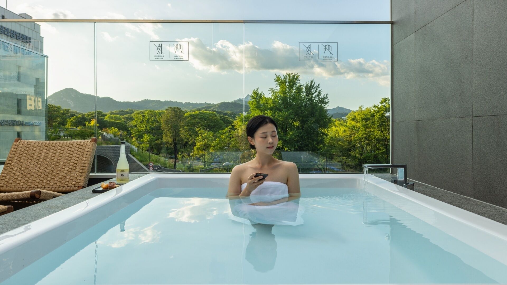 Une personne dans un bain à remous, avec vue sur un paysage montagneux, une bouteille et une chaise.