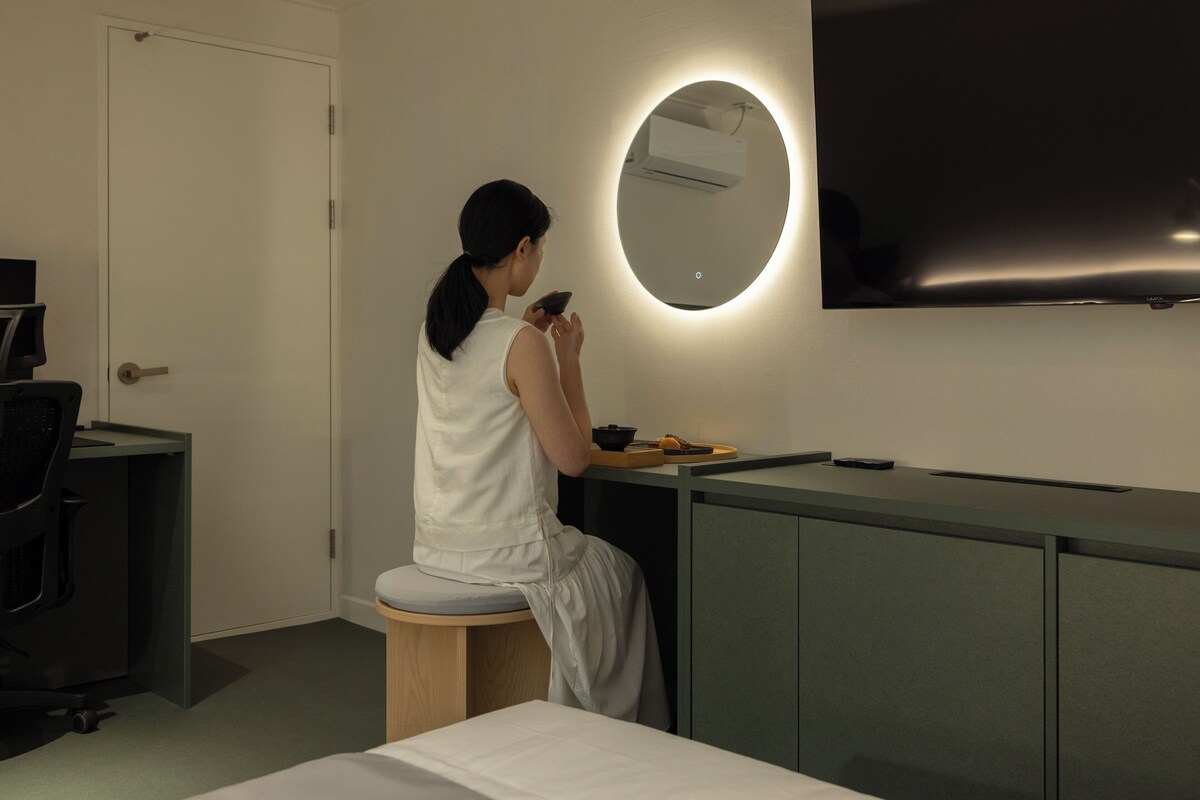 Una habitación con escritorio, silla, cama, espejo y televisor de pantalla plana.